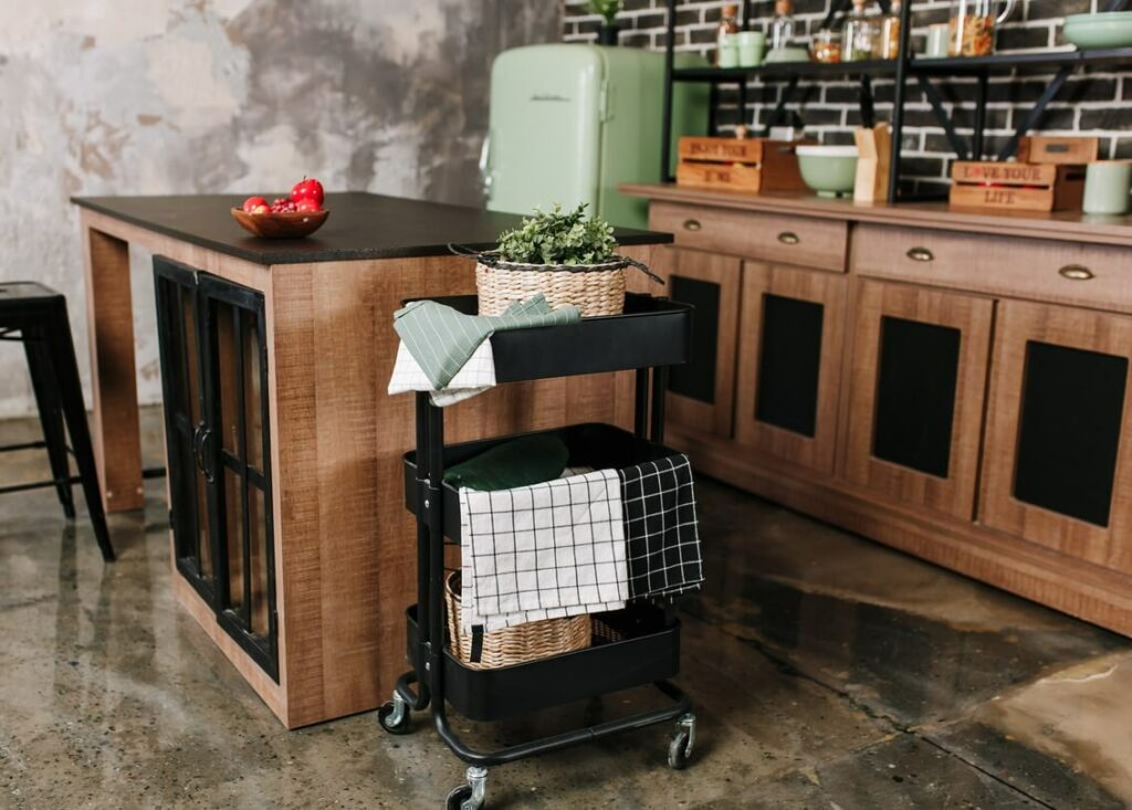 A black rolling cart holds towels and baskets next to a kitchen counter.