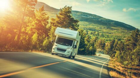 A camper van driving on a road through hills and trees at dusk.